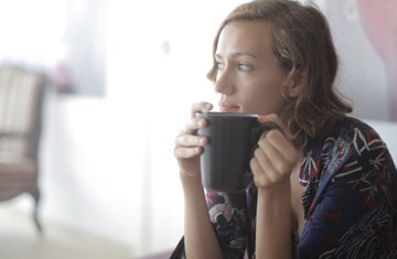 White woman sitting in corner of room holding a large mug of tea