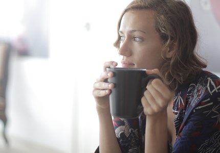 White woman sitting in corner of room holding a large mug of tea