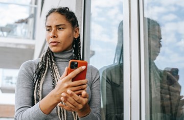 Concerned young black woman standing outside glass door holding a mobile phone