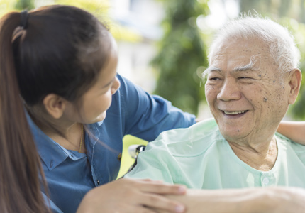 An older person in green smiles with their carer.